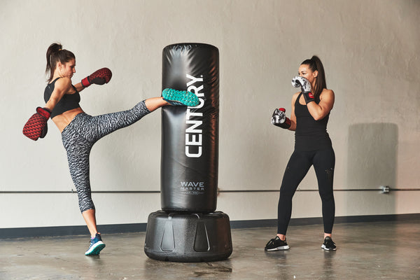 Two women kicking a freestanding bag