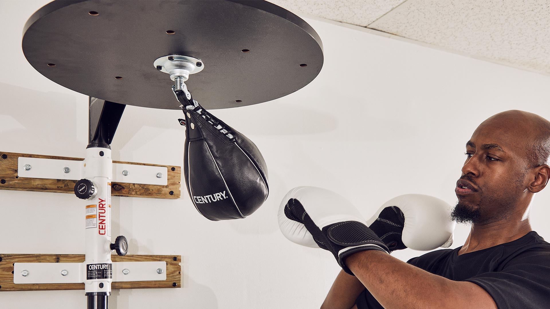 man hitting century hanging speed bag wearing boxing gloves